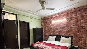 A bedroom with a bed, a ceiling fan, a brick wall, and a door. - Staylo Jaggannath Stays (New Delhi)