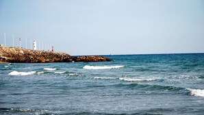 Eine felsige Küste mit einem Leuchtturm, Wellen und einem klaren Himmel.