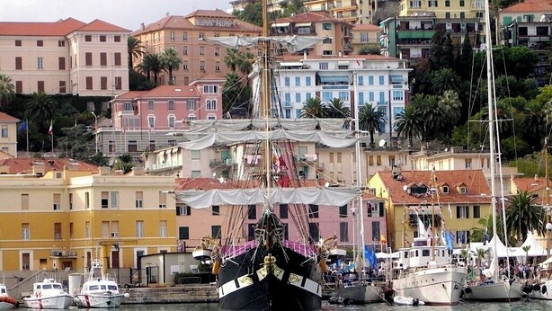 Ein Hafen mit einem großen Segelschiff, umgeben von bunten Gebäuden und anderen Booten.