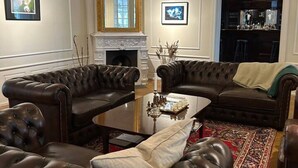 A living room with leather sofas, a fireplace, a chandelier, and a bar area. - Mockelsnas Manor Manor Gardenview Queen Room (Diö)