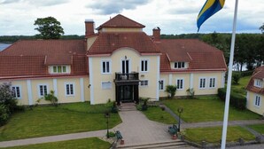 A large, two-story building with a symmetrical facade, a central entrance, and a flagpole with a flag. - Mockelsnas Manor Manor Gardenview Queen Room (Diö)