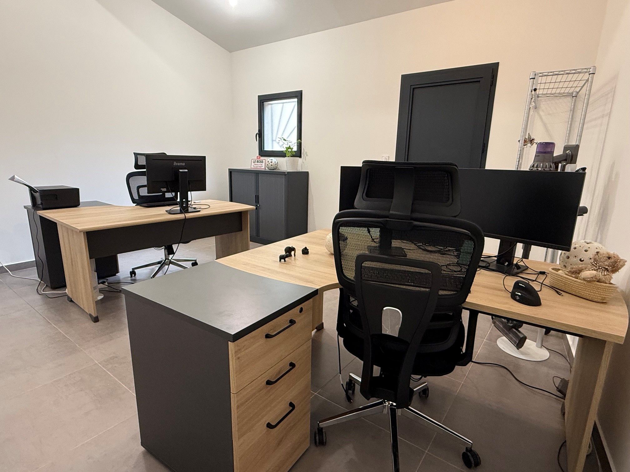 Un espacio de oficina moderno con dos escritorios, sillas y monitores de computadora.