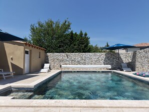 Une piscine avec des murs en pierre, une porte et deux chaises longues.