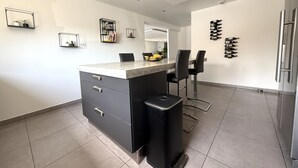A modern kitchen with a central island, black chairs, a refrigerator, and wine bottles on the wall. - 12-Person Villa A/C Heated Pool office close Aix Provence (Salon-de-Provence)