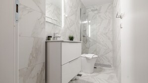 A modern bathroom with a marble floor, a white vanity, a glass shower enclosure, and a toilet. - Phaedrus Living: Skiathos Luxury Residences Green (Skiathos)