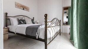 A bed with a metal frame, a bedside table, a wall-mounted artwork, and a mirror with a green curtain. - Phaedrus Living: Skiathos Luxury Residences Green (Skiathos)