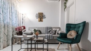 A modern living room with a grey sofa, a green armchair, a coffee table, and a wall-mounted painting. - Phaedrus Living: Skiathos Luxury Residences Green (Skiathos)
