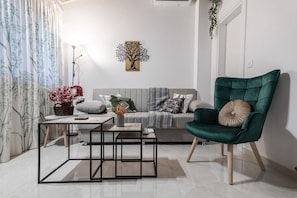 A modern living room with a grey sofa, a green armchair, a coffee table, and a wall-mounted painting. - Phaedrus Living: Skiathos Luxury Residences Green (Skiathos)