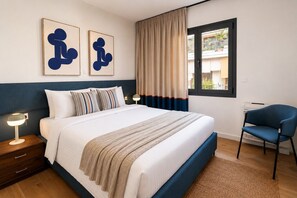A bedroom with a bed, bedside tables, a chair, a window with curtains, and artwork on the wall. - LIV - Upscale Athenian Apartment 4B (Athens)