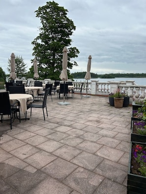 An outdoor patio with tables and chairs, umbrellas, and a view of a lake.