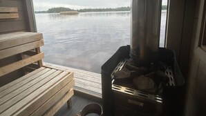 A sauna room with wooden benches, a sauna stove, and a view of a lake. - Mockelsnas Manor Lakeview Queen Room and Lounge (Diö)