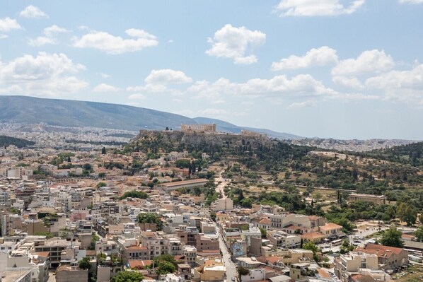 A cityscape with a prominent ancient fortress on a hill, surrounded by residential buildings and greenery. - LIV - Upscale Athenian Apartment 4C (Athens)