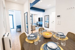 Ein Essbereich mit einem runden Tisch, gedeckt für sechs Personen, einer großen Zitronenschale sowie einem modernen Interieur mit blauer Akzentwand und sichtbarer Klimaanlage.