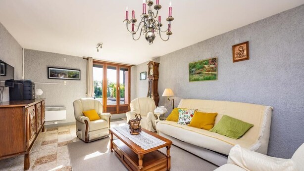 Ein Wohnzimmer mit einer Couch, Sesseln, einem Couchtisch, einer Kandelaber, einem Kamin und einem Fernseher.