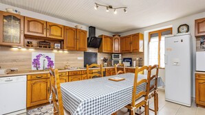 Eine Küche mit Holzausstattung, einem Esstisch mit kariertem Tischläufer, einem Kühlschrank und einer Mikrowelle.