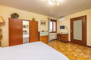 Ein Schlafzimmer mit Bett, Holzschrank, Schreibtisch, Stuhl und einem Fenster mit Vorhängen.