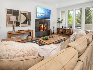 Ein Wohnzimmer mit Kamin, Fernseher und einem großen Fenster mit Blick auf Bäume.