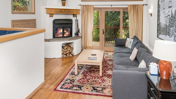 Ein Wohnzimmer mit Kamin, einer Couch, einem Couchtisch und Blick ins Grüne durch große Fenster.