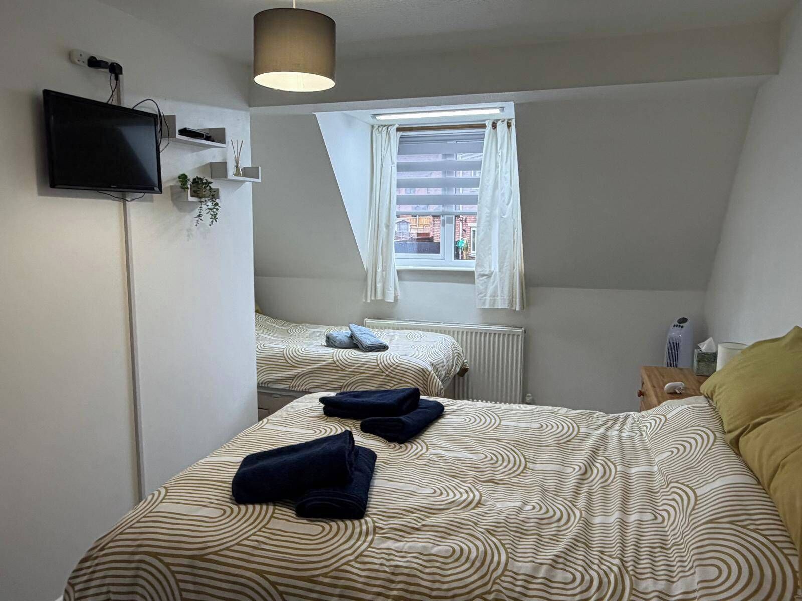 A bedroom with two beds, a TV, a radiator, and a window with curtains.