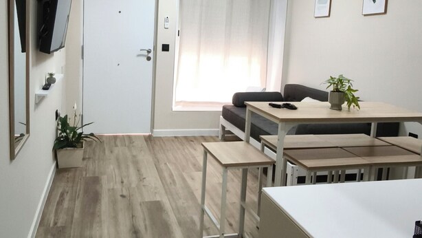 Ett kompakt bostadsutrymme med ett litet kök, en matplats och en dörr som leder till ett annat rum.