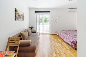 A room with a brown sofa, a wooden chair, a bed with a patterned bedspread, a small table with a teapot, and a painting on the wall. - Cozy studio apartment in charming Becici (Bečići)