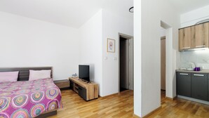Ein Schlafzimmer mit einem Bett, einem Fernseher, einem kleinen Holztisch und einer Küchenzeile mit Schränken und einer Arbeitsfläche.
