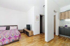 Ein Schlafzimmer mit einem Bett, einem Fernseher, einem kleinen Holztisch und einer Küchenzeile mit Schränken und einer Arbeitsfläche.