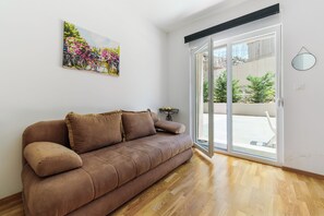 Ein Zimmer mit einem braunen Sofa, einem Blumenbild, einer Schiebetür und einem kleinen Tisch.