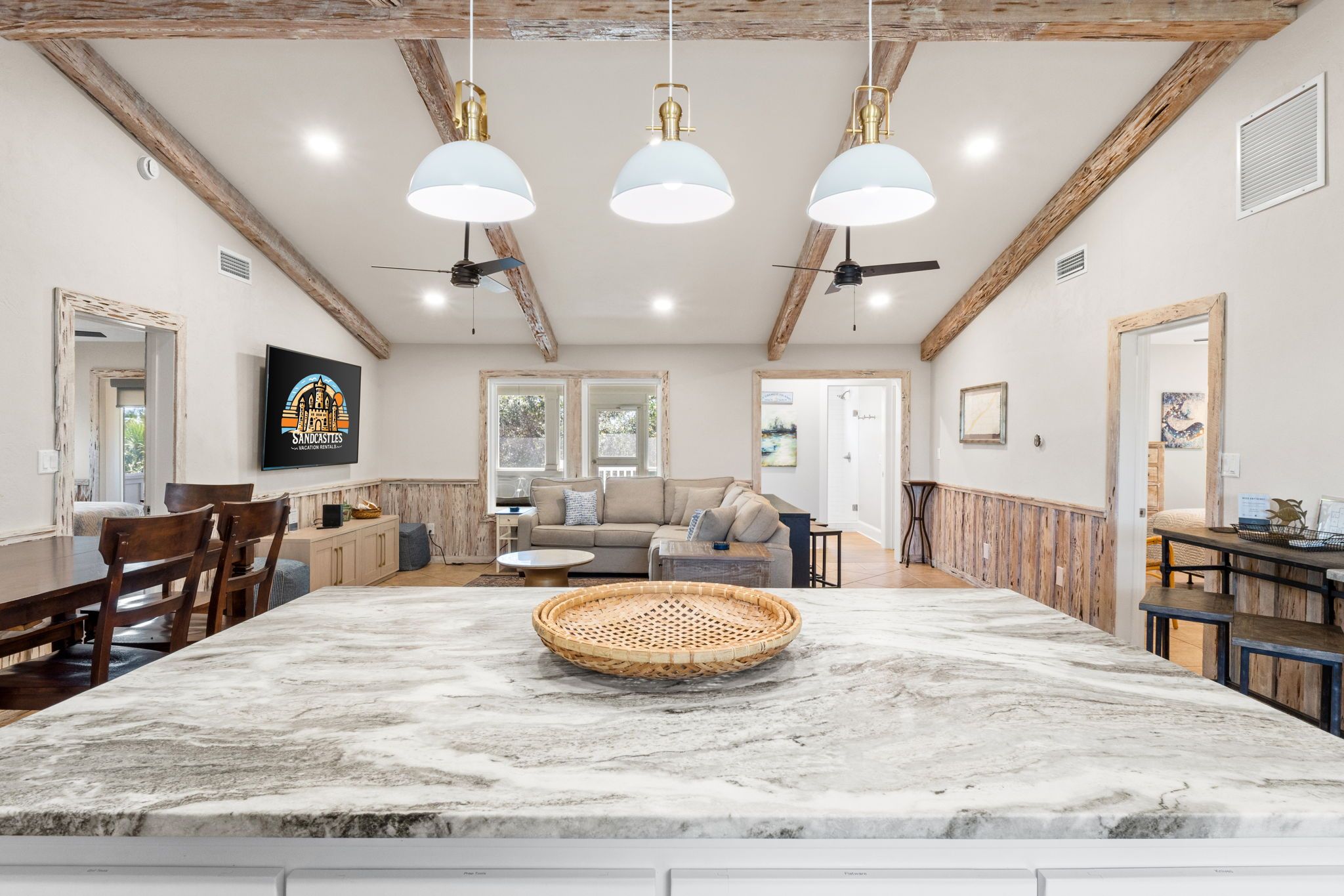 A spacious kitchen with a marble island, wooden beams, and pendant lighting.