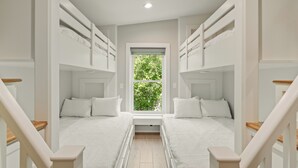 Ein Zimmer mit zwei Etagenbetten, einem Fenster mit Blick auf Grünflächen und einer Holztreppe.