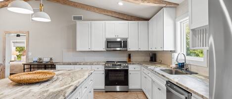 A modern kitchen with white cabinets, a stainless steel oven, and a marble countertop.