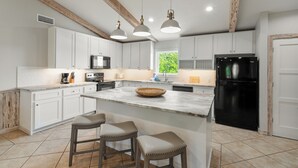 Eine moderne Küche mit weißen Schränken, einem schwarzen Kühlschrank und einer zentralen Kochinsel mit Sitzgelegenheiten.