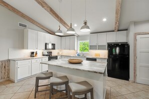 A modern kitchen with white cabinets, a black refrigerator, and a central island with stools. - About Time-3BR/4BA Pet Friendly,Private Pool (St. George Island)