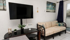 Un salon avec un canapé, un téléviseur, une petite table sur laquelle est posée une plante, et un panneau indiquant la direction de la plage.