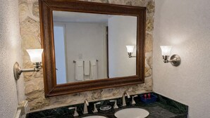 Une salle de bain avec un mur en pierre, un miroir encadré en bois, deux vasques avec des plans de travail en marbre et des appliques murales.