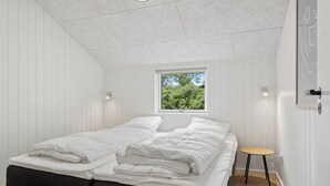 A bedroom with a bed, a small table, a window, and a door. - Newly renovated holiday home near the water (Hadsund)
