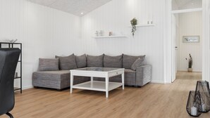 A modern living room with a sectional sofa, a glass-top coffee table, and a black chair. - Newly renovated holiday home near the water (Hadsund)