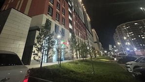 Un edificio de gran altura con varios pisos, ventanas iluminadas y un estacionamiento con coches.