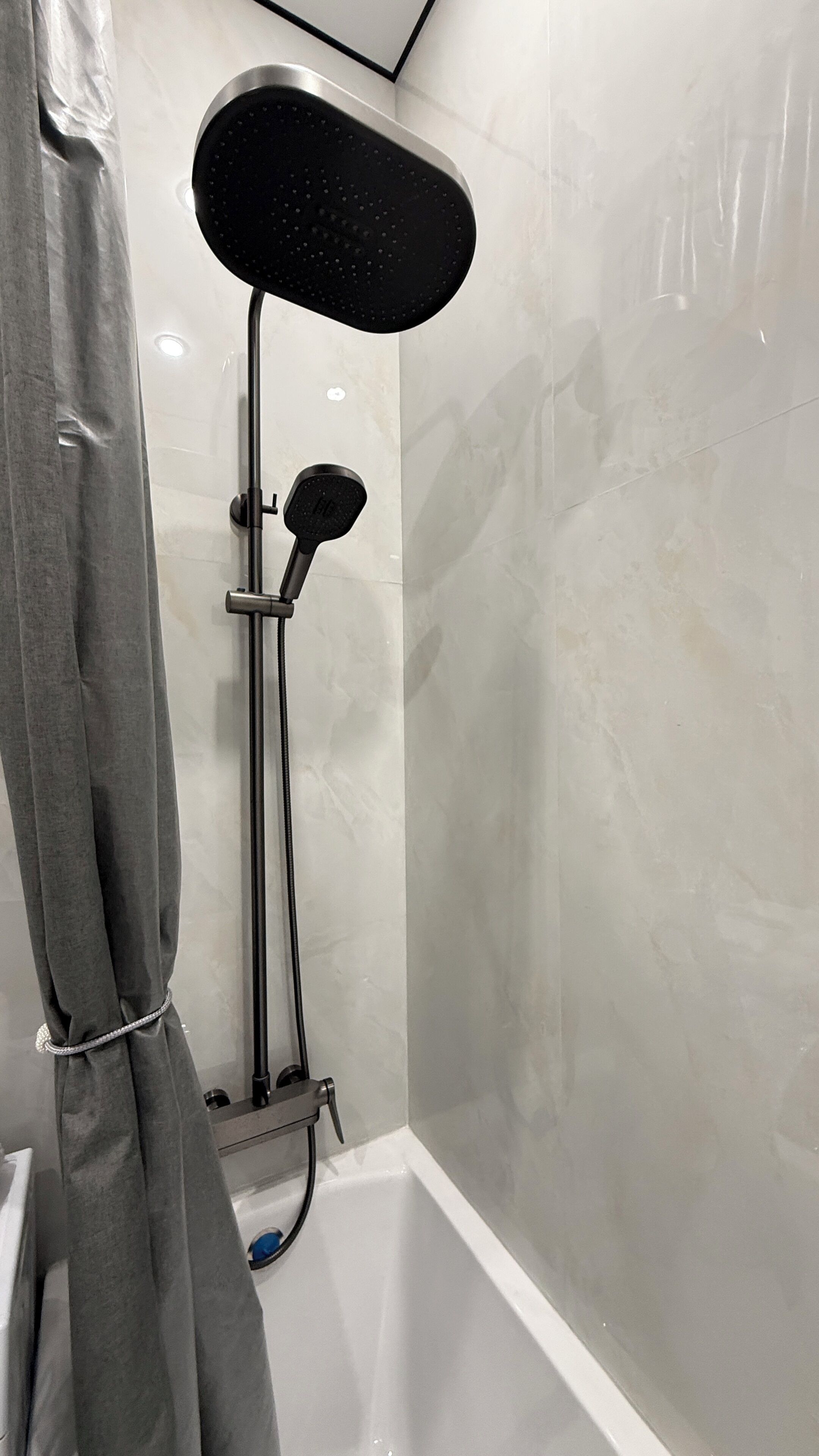 A shower with a handheld showerhead, a wall-mounted control, and a curtain.