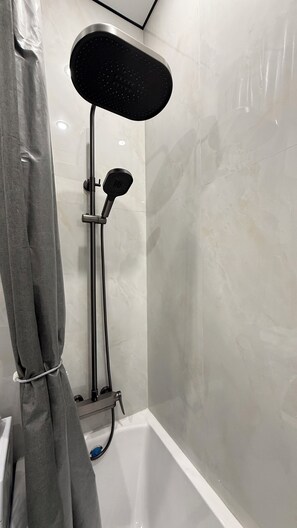 Une douche équipée d’un pommeau de douche à main et d’un panneau de commande fixé au mur.