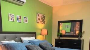 Un letto rifatto con una coperta blu, una testiera grigia e un condizionatore d'aria a parete.