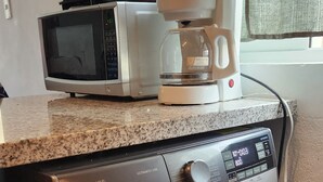Een praktische keuken met een wasmachine, een magnetron en een koffiezetapparaat op het aanrecht.