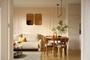A living room with a sofa, a dining table with chairs, a small side table, and a plant. - Polka Bright 2-Bed by Fragola Apartments (Kraków)