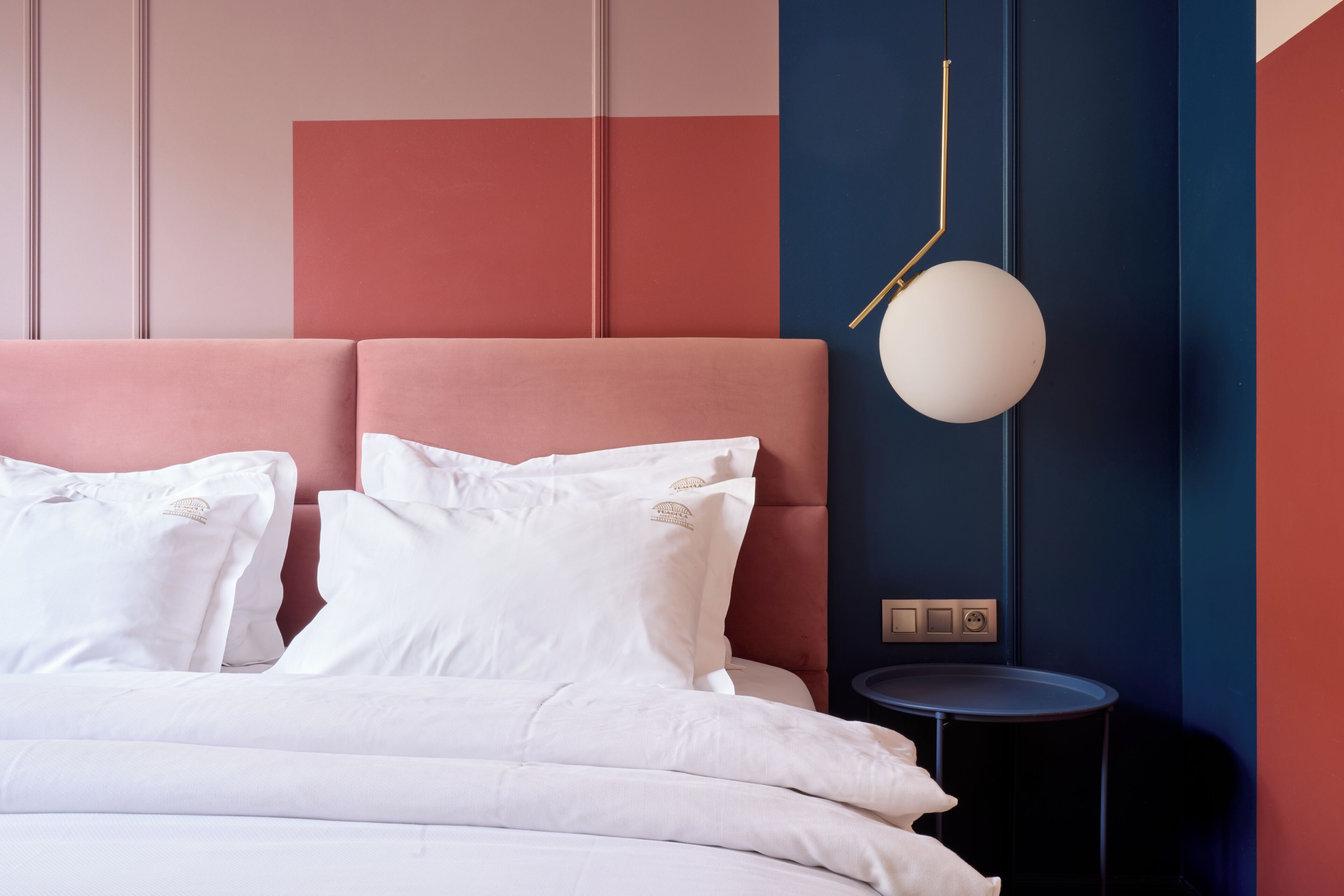 A bed with white bedding, a pink headboard, and a round wall-mounted light fixture.