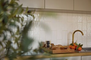 Eine Küche mit weißen Fliesen, einem Holzschneidebrett mit Brot und Orangen sowie einem goldenen Wasserhahn.