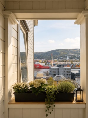 Une vue sur la ville, avec ses bâtiments, un navire rouge et une colline en arrière-plan, telle qu'elle apparaît à travers une fenêtre.