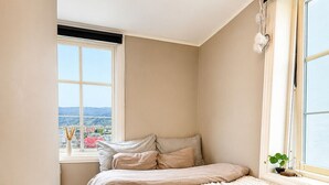 Una camera da letto con un'ampia finestra, un letto con coperta trapuntata e vista sulla città.