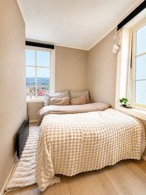 Une chambre avec une grande fenêtre, un lit recouvert d’une couverture à motifs, et une vue sur la ville.