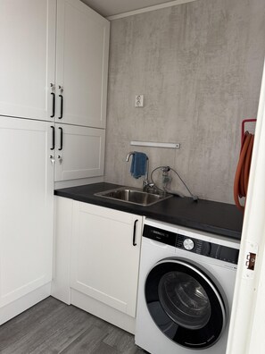 A compact kitchen with white cabinets, a built-in washing machine, a sink, and a towel rack.