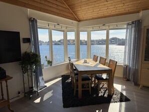 Un espace repas comprenant une table et des chaises, de grandes fenĂȘtres donnant sur un lac, et un plafond avec des poutres en bois.